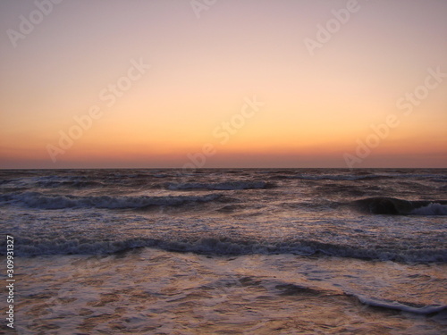 Landscape of vast sea horizon against a background of blue sky decorated with rainbow shades of summer dawn.