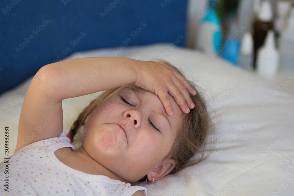 Caucasian child of three age simulating illness lying in bed holding her hand on head with shut eyes