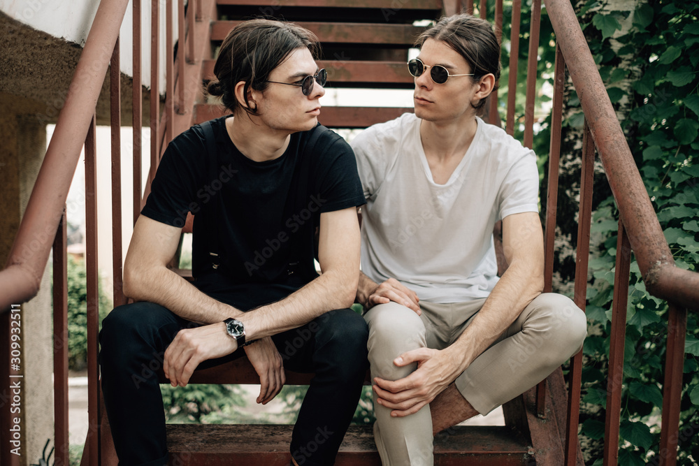 Obraz premium Two Stylish Twins Brothers Sitting on the Stairs