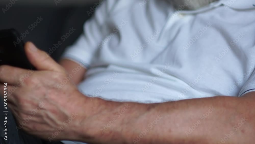 Focused elderly man using his smartphone on a sofa. Close-up, hands and face. A man wears glasses and a gray beard, an elderly man and a smartphone Focused elderly man using his smartphone on a sofa. Close-up, hands and face. A man wears glasses and a gray beard, an elderly man and a smartphone