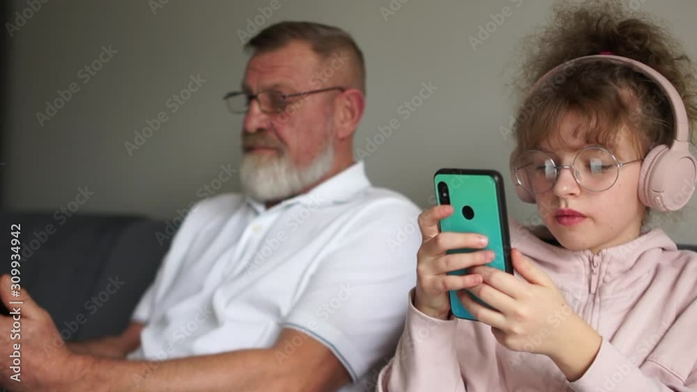 Grandfather and granddaughter of a teenager are sitting next to the couch and everyone is looking at their smartphone. Disunity of people, harm to smartphones. Family Lifestyle