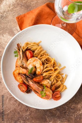 Mediterranean cuisine, pasta with king prawns, brown stone background.