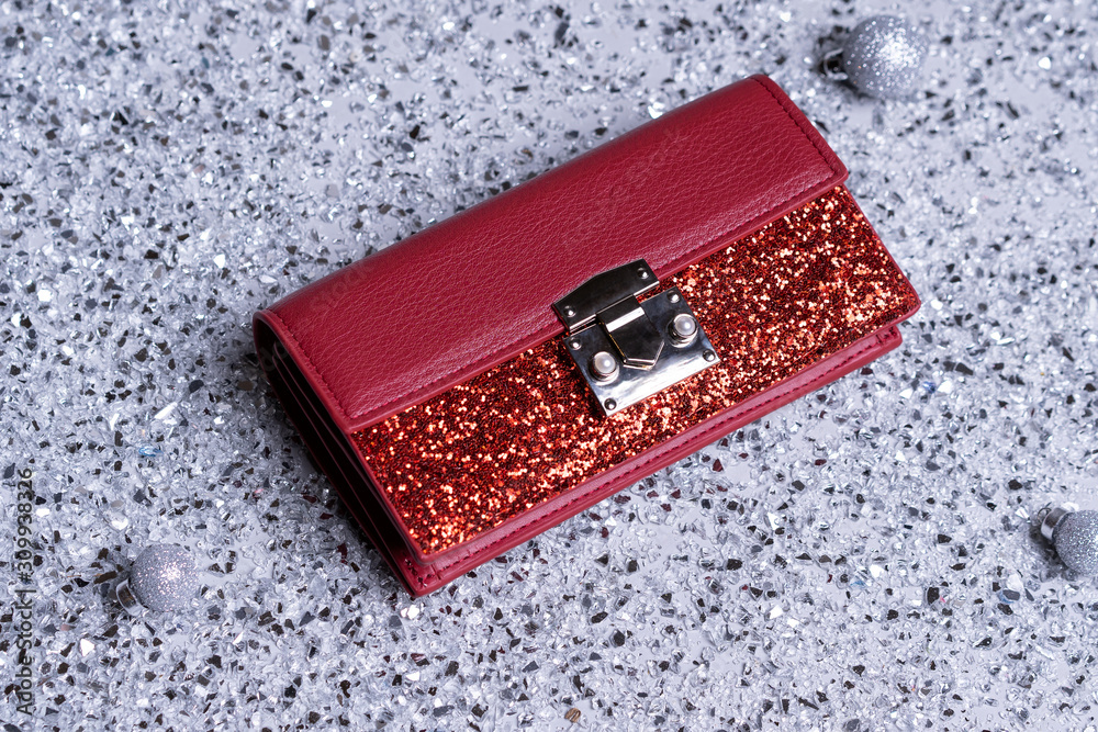 Red little female clutch bag with sequins. Brilliant, festive for a party. lies on a gray background with broken glass. Accessories for a female image Red little female clutch bag with sequins. Brilliant, festive for a party. lies on a gray background with broken glass. Accessories for a female image