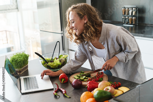 Happy young woman making a salad at the kitchen photo