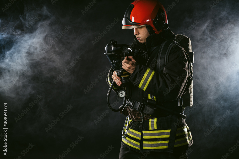 Naklejka premium young adult firefighter saving people from fire wearing uniform and helmet, holding fire fighting equipment