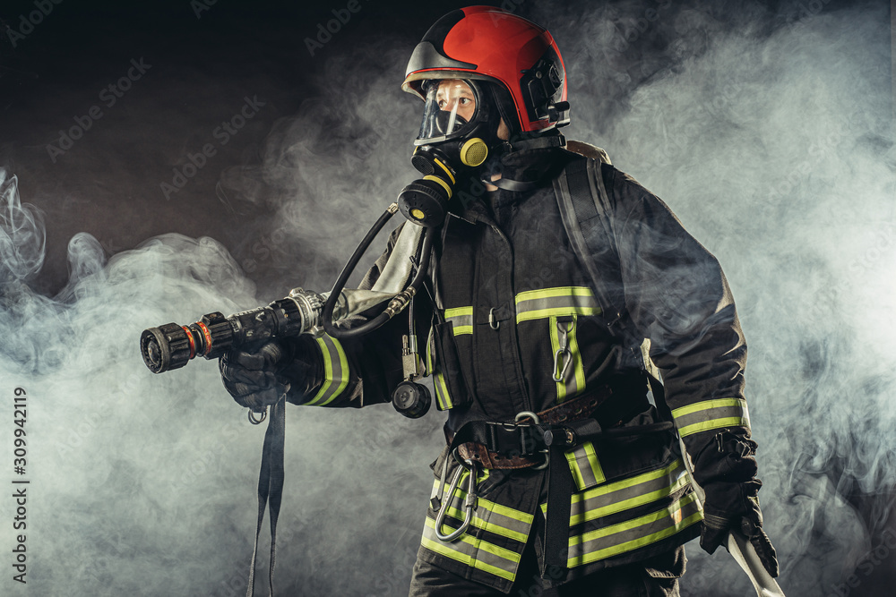 Obraz premium young firefighter in uniform stand in smoky background wearing uniform, safety concept