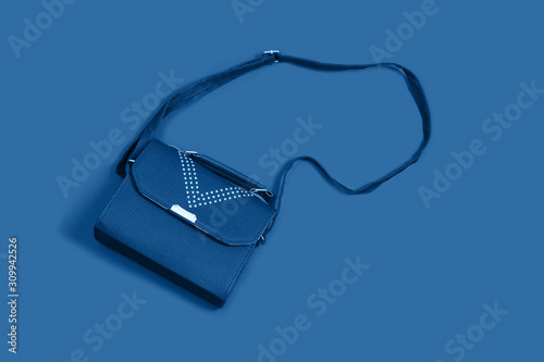 Woman leather small handbag clutch on blue background. Minimalism in women's things.
