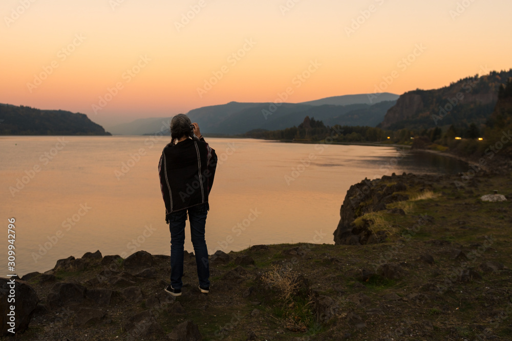 Young woman with poncho takes photographs of the sunset at the Corbett lookout on the Columbia River, Oregon