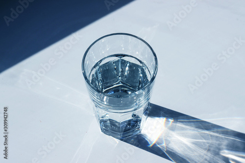 Water glass with strong shadows on white background, toned in 2020 classic blue color