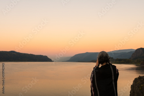A young woman with poncho takes photographs of the sunset at the Corbett lookout on the Columbia River, Oregon