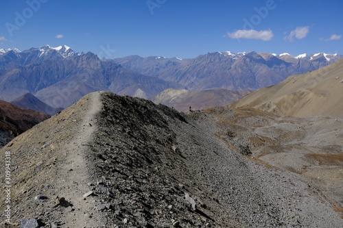 Harsh desert mountain scenery of Mustang land on trail from Thorung La Pass to Muktinath, Himalaya, Nepal. Small silhouette of tourist on ridge. During trekking around Annapurna. photo