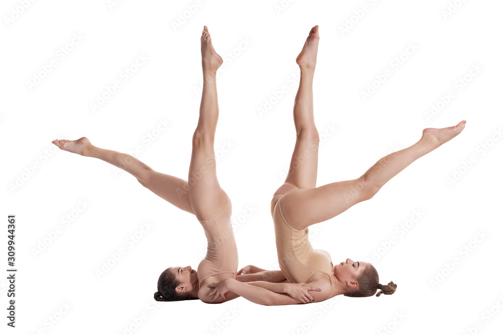 Two flexible girls gymnasts in beige leotards are performing exercises upside down using support and posing isolated on white background. Close-up. Two flexible girls gymnasts in beige leotards are performing exercises upside down using support and posing isolated on white background. Close-up.
