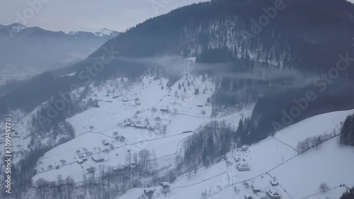 Calm and cosy fairy-tale village Kryvorivnia covered with snow in the Carpathians mountains, aerial view. Clouds and morning fog in moountains photo