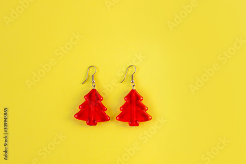 Red trendy earrings in the form of red Christmas trees on yellow pastel background. Minimal flatlay. Womens unusual silver jewelry closeup. Girls accessories, holidays event look, social media banner.