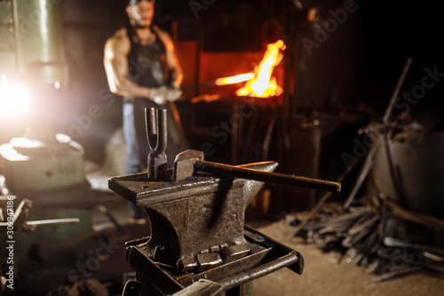 close-up of hammer and other instruments  equipment for forging  blacksmithing. muscular young man near furnace in the background