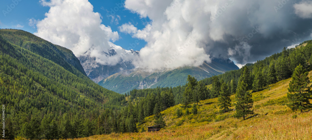 Mountain valley, green forests. Sunny summer day, blue sky with clouds, thundercloud. Travel and vacation in the mountains.