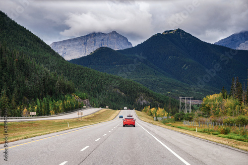 Red car driving on highway with rocky mountains in national park