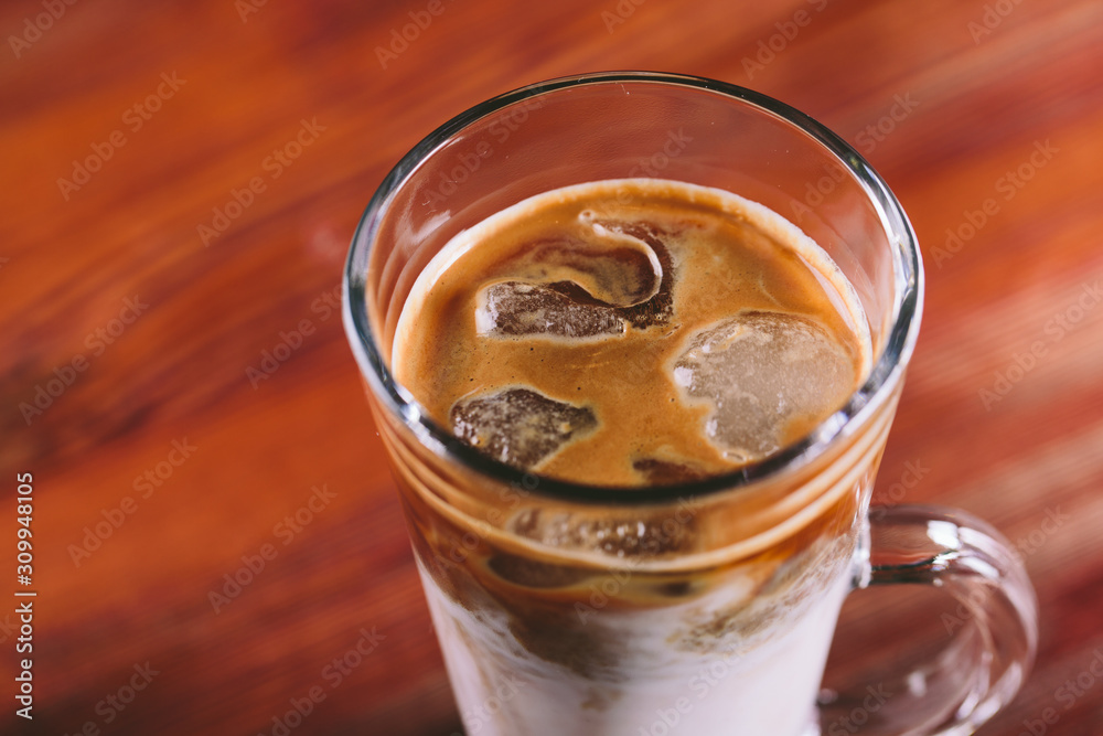 The glass cup of latte with ice on wooden table The glass cup of latte with ice on wooden table