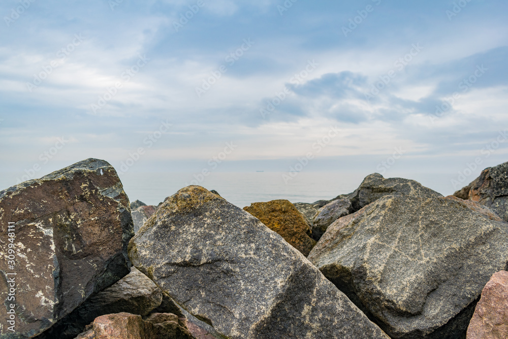 Granite revetment or seawall on the shore. Huge stones to protect beach from erosion. Prevent disaster. Copy space. Blue cloudy sky. Granite revetment or seawall on the shore. Huge stones to protect beach from erosion. Prevent disaster. Copy space. Blue cloudy sky.