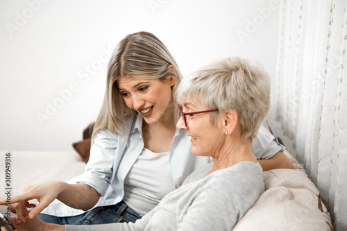 A senior blonde woman has a tablet in her hand while a young woman explains how to use the internet,iptv, social networks and online shopping. She is very curious and wants to learn.