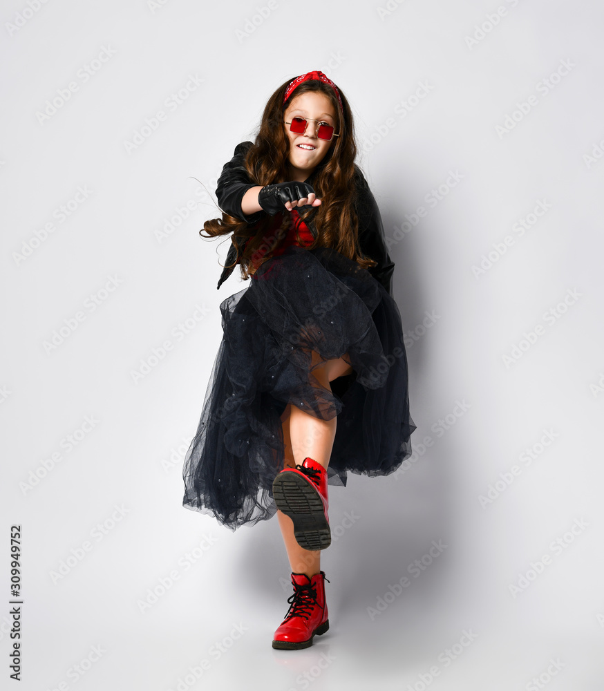 Young positive plus size girl model in bright rock style clothing, red boots and square glasses dancing over white background