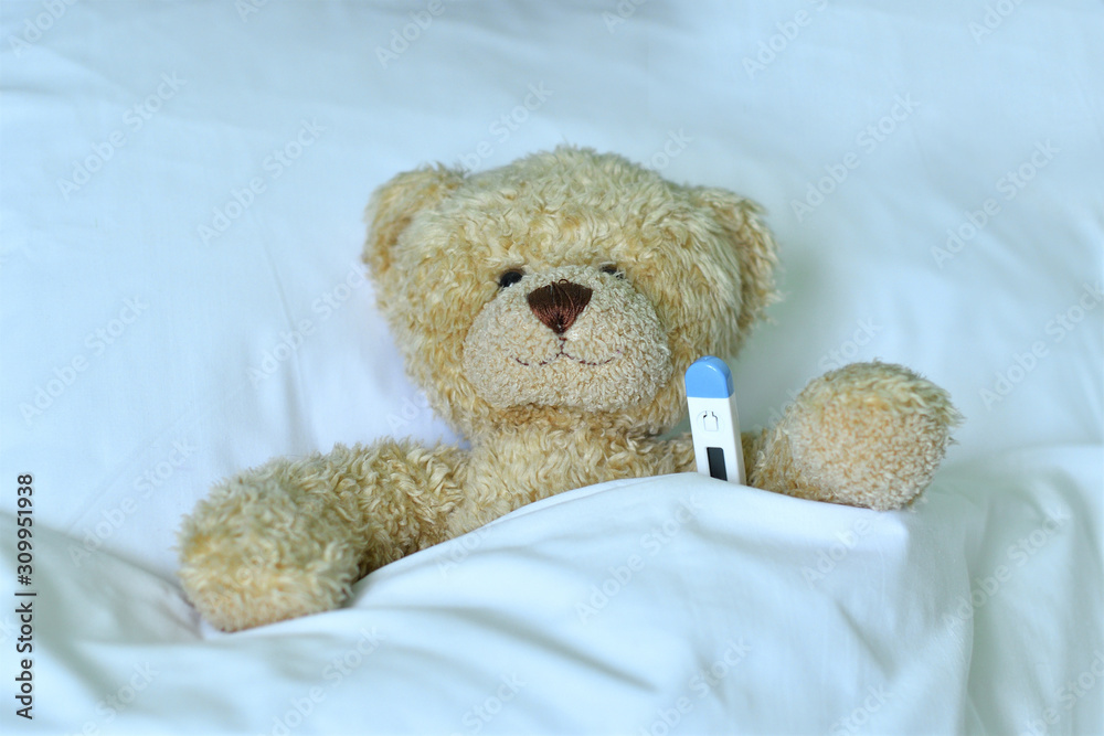 Teddy bear with a electronic thermometer in bed