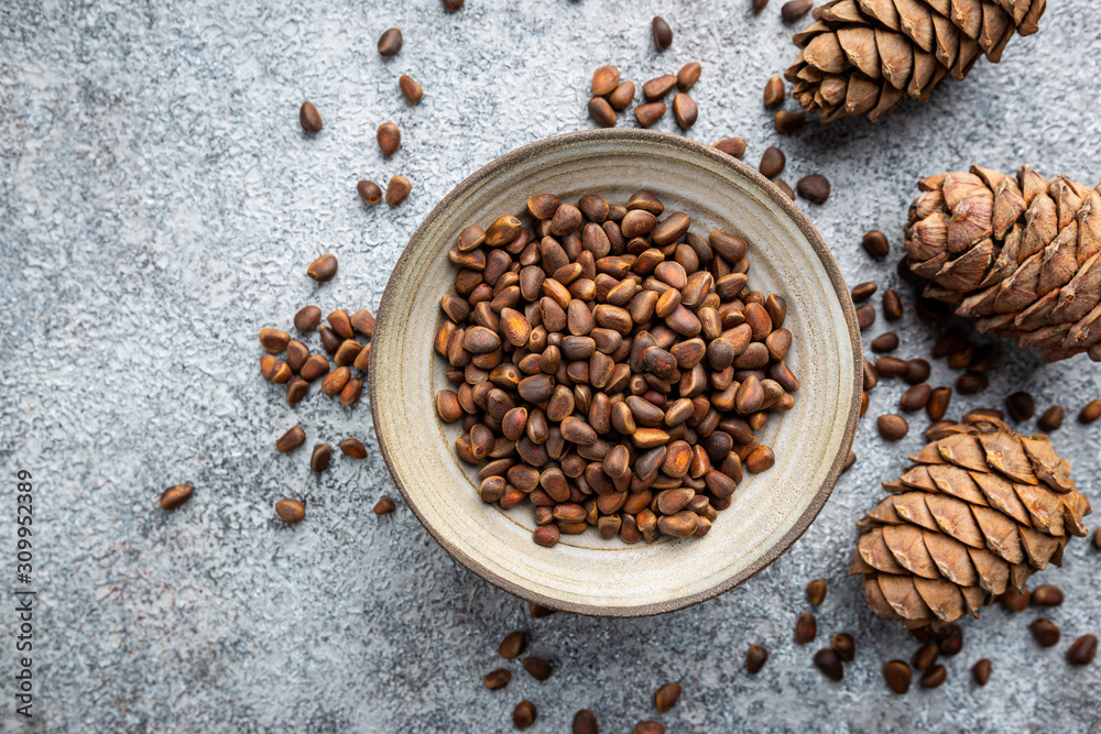 Cedar or pine nuts in a bowl with cones on gray background, top view Cedar or pine nuts in a bowl with cones on gray background, top view
