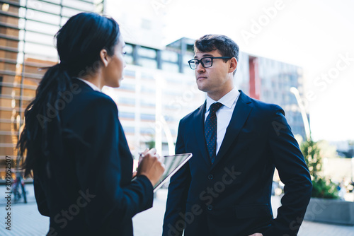 Man talking to female worker with tablet Formal confident man in glasses having professional discussion with young ethnic woman conducting survey and using modern tablet on street