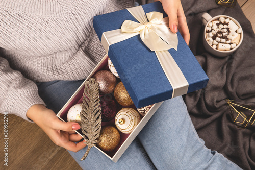 Christmas balls and decor in a box in the hands of a girl sitting on the floor.