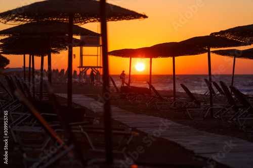 wooden walkway on beach among sun loungers and straw umbrellas at sunset , Greece, Rhodes.