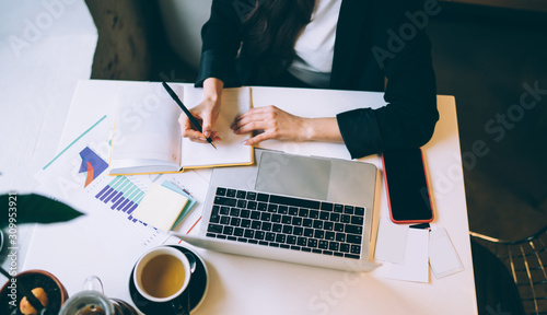 Tableau sur toile Professional businesswoman revising graphs and taking notes while working on lap