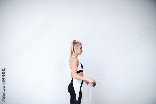 Girl in sportswear rolls a yoga mat before training on white background.