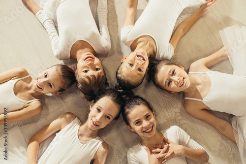 charming cute ballerinas beginners lying on floor in circle and looking at camera, happy caucasian ballerinas in tutu skirts © alfa27
