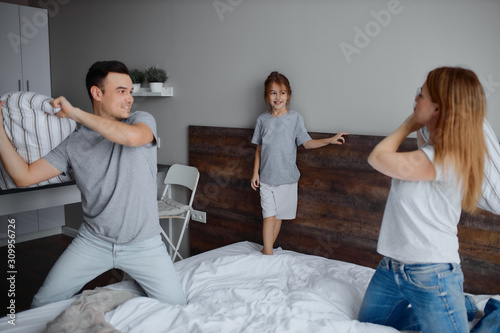 happy caucasian family, mother father and child girl fight play with pillows on bed, cheerful family concept