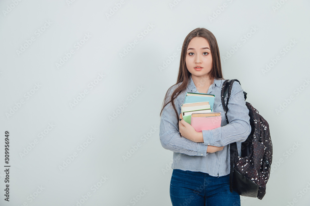 Happy casual asian girl student with backpack standing holding a stack of books close to her chest, looking seriously at the camera. Happy casual asian girl student with backpack standing holding a stack of books close to her chest, looking seriously at the camera.