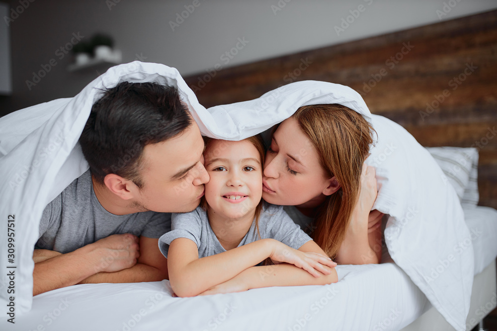 lovely family on bed, spend free time together at morning, portrait of smiling positive family under blanket, three members of family, daughter in the center