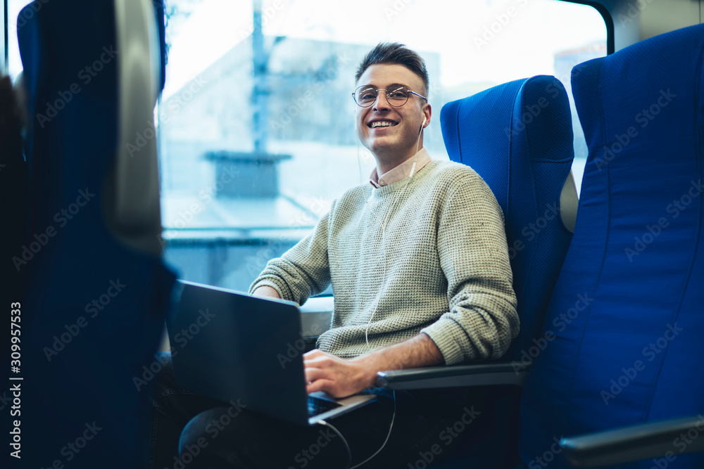 Smiling modern traveler with laptop riding in train