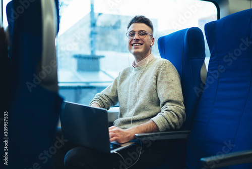 Smiling modern traveler with laptop riding in train