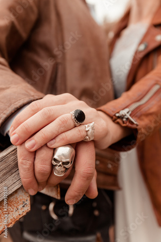 Romance of bikers. Man and woman hold hands. Hands with rings. Leather jackets. Autumn wedding in nature