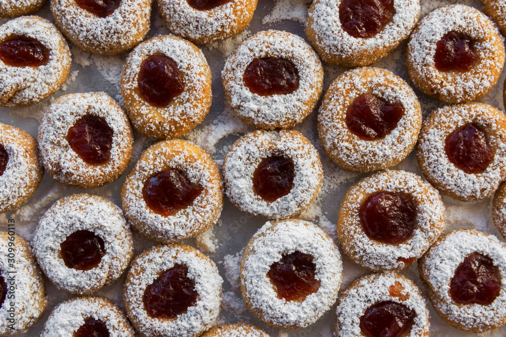 Christmas shortbread thumbprint cookies with strawberry jam powdered with castor sugar on white parchment paper on baking tray. Festive atmosphere holiday pastry baking concept Christmas shortbread thumbprint cookies with strawberry jam powdered with castor sugar on white parchment paper on baking tray. Festive atmosphere holiday pastry baking concept