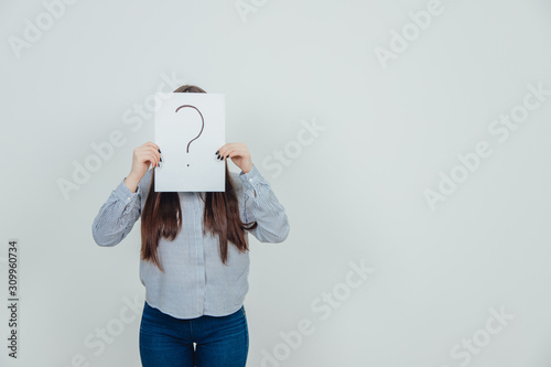 Fotografie Inquisitive asian student girl hiding her face behind a sheet of paper with question mark written on it