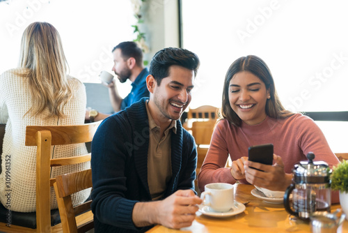 Couple Checking Photos On Smartphone At Cafe