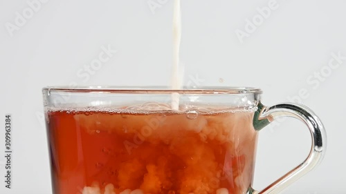 Close up pouring milk in glass cup of black tea