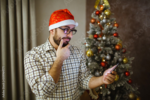 Portrait of a tall man holding the phone in his hand, near a Christmas tree.