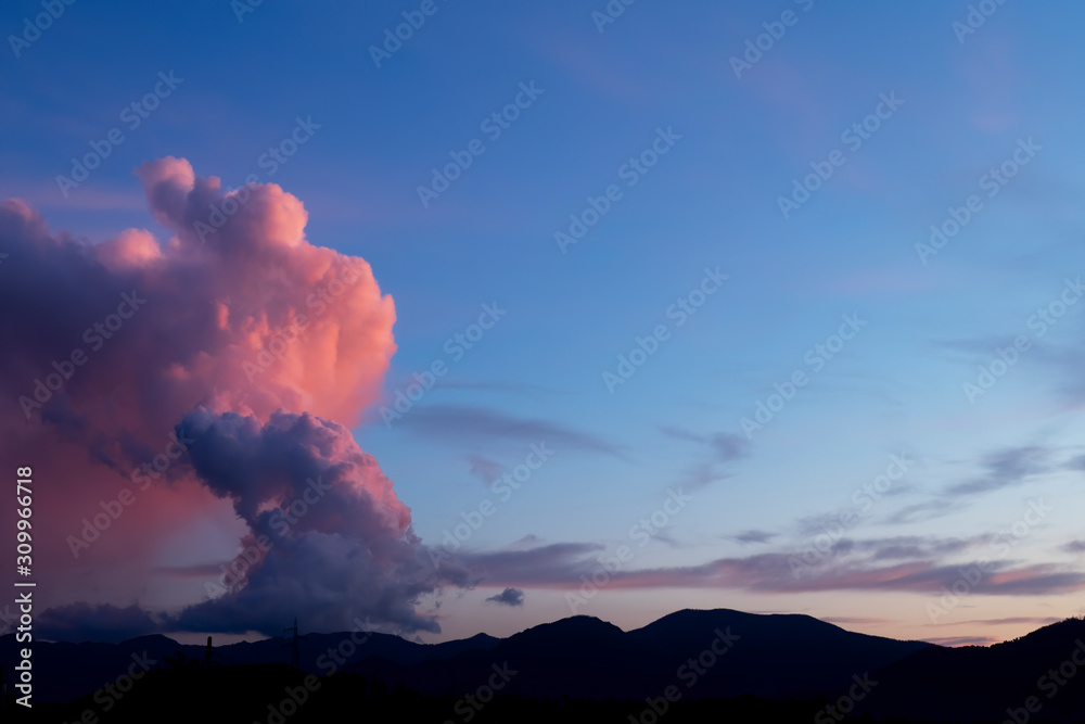 Cumulonimbus, hailstorm cloud over Lunigiana, Italy. December 2019. Towering column at sunset with red sky.