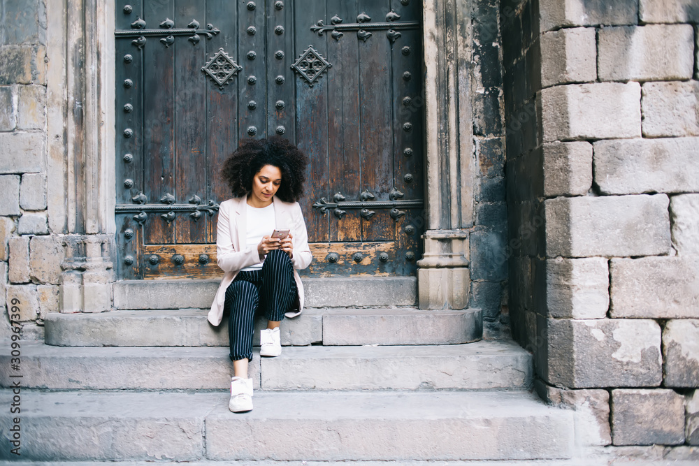 Black woman surfing Internet on smartphone and sitting on stone steps
