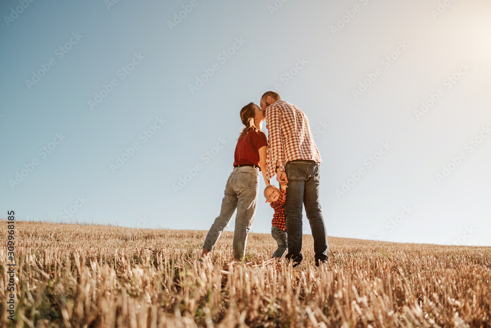 Happy Young Family Mom and Dad with Their Little Son Enjoying Summer Weekend Picnic Outside the City in the Field at Sunny Day Sunset, Vacation Time Concept Happy Young Family Mom and Dad with Their Little Son Enjoying Summer Weekend Picnic Outside the City in the Field at Sunny Day Sunset, Vacation Time Concept