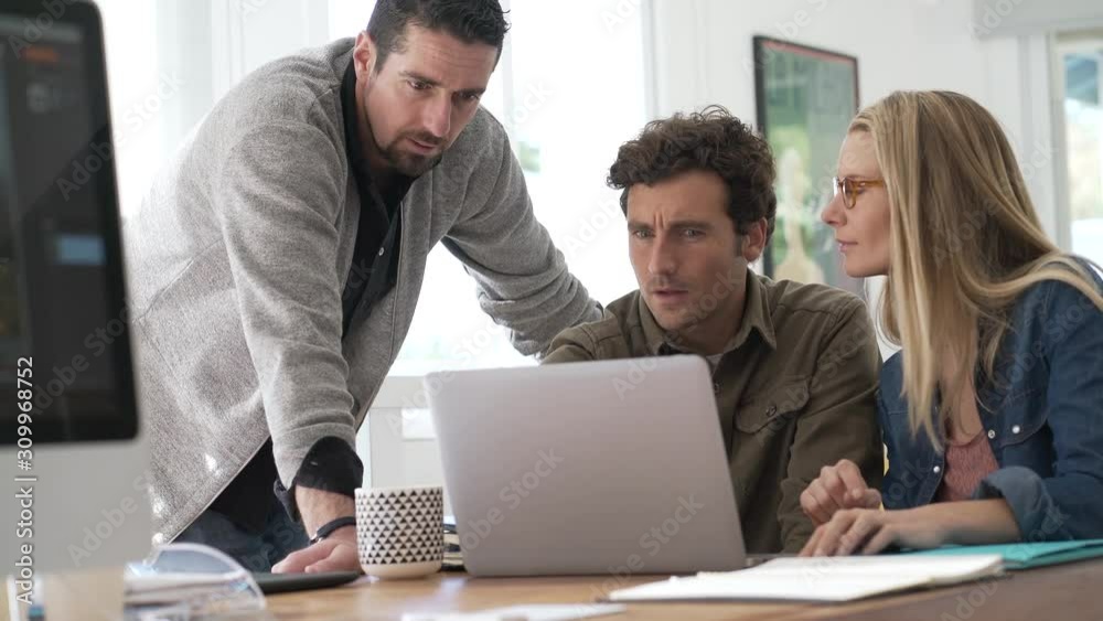 Co-workers gathering in office and using laptop Co-workers gathering in office and using laptop