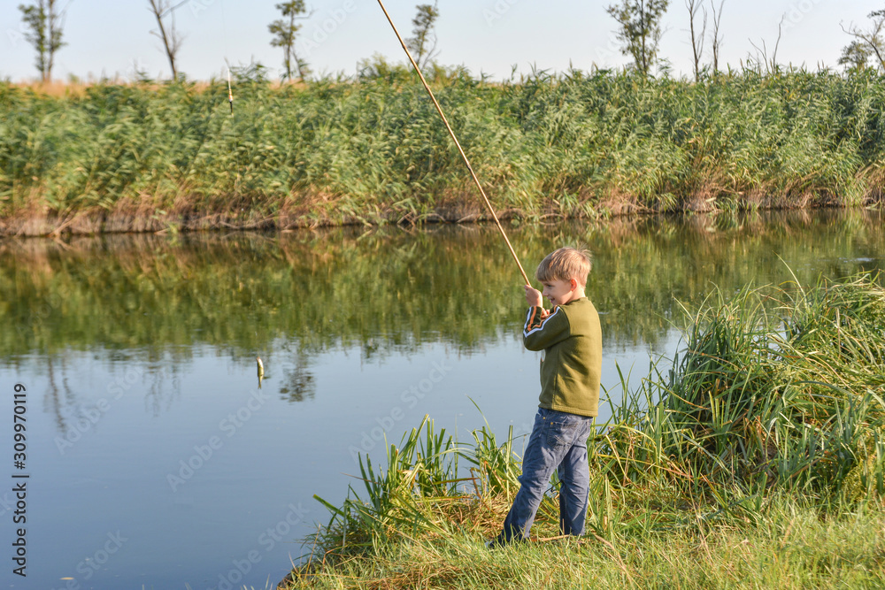 A joyful and happy boy rejoices at his first catch of fish on a fishing rod on the river. A joyful and happy boy rejoices at his first catch of fish on a fishing rod on the river.