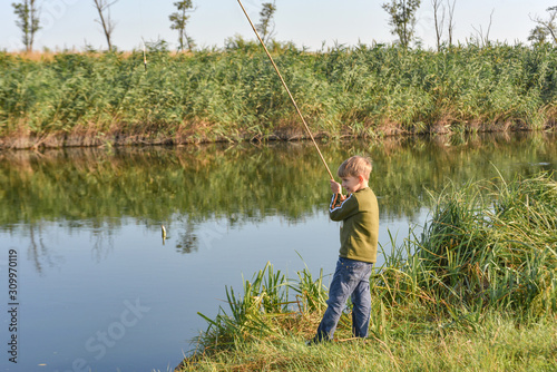 A joyful and happy boy rejoices at his first catch of fish on a fishing rod on the river.